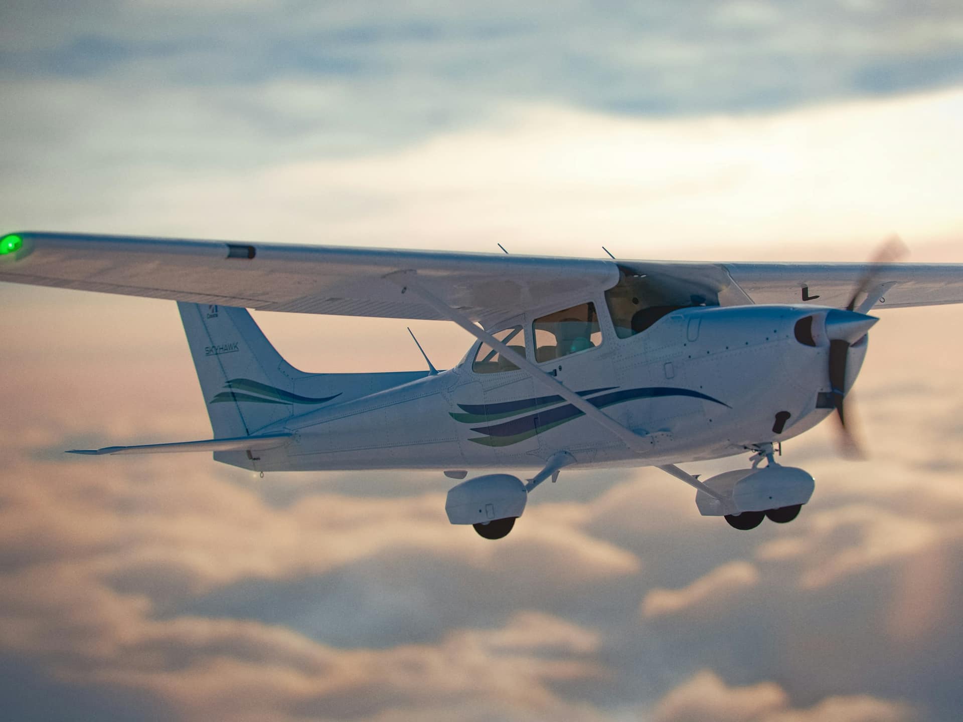 A high-wing single-engine airplane flying above a layer of soft evening cloud